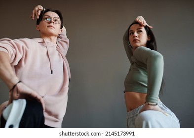 Two active teenagers keeping their arms over heads while training new movements of vogue dancing in modern studio or dance hall