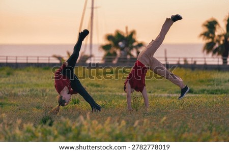 Two active women practicing synchronized cartwheels and dynamic gymnastics routines in an open field at sunset