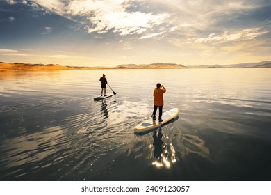 Two active young tourists are walks on stand up paddle sup boards at calm mongolian lake in sandy dunes - Powered by Shutterstock