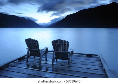 Two Adirondack Chairs On A Deck  At Sunset