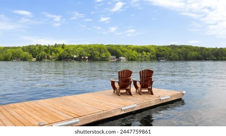 Two Adirondack chairs rest on a wooden dock in sunny Muskoka, Canada, facing a tranquil lake. Cottages nestled among trees line the shore across the water, completing the scene. - Powered by Shutterstock