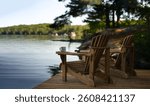Two Adirondack chairs sit on a cottage dock, facing a calm Muskoka lake with cabins in view on a sunny summer morning. A coffee tin on one arm reads "Life is better at the Cottage".