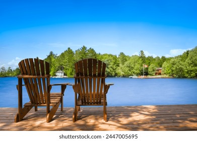 Two Adirondack chairs sit on a wooden dock, overlooking a tranquil lake. On the opposite shore, a white cottage is nestled among lush green trees, with a boat docked in front. - Powered by Shutterstock