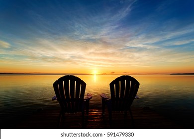 Two adirondack chairs waiting at the end of a dock to enjoy the early morning sunrise