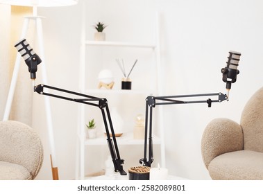 Two adjustable microphone stands are set up in a bright room with minimalist decor, ready for a podcast recording session. The space features soft furnishings and greenery.