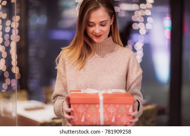 Two Adolescent Women Sitting In A Fancy Restourant, Going Through The Menue, While Drinking Some Red Wine, Talking, Gossiping And Unwrapping Their Christmass Presents And Looking At Their Phones. 