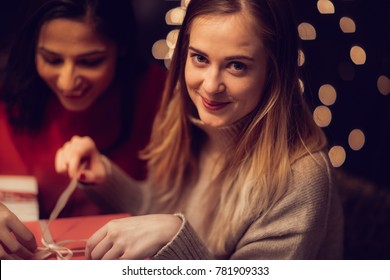 Two Adolescent Women Sitting In A Fancy Restourant, Going Through The Menue, While Drinking Some Red Wine, Talking, Gossiping And Unwrapping Their Christmass Presents And Looking At Their Phones. 