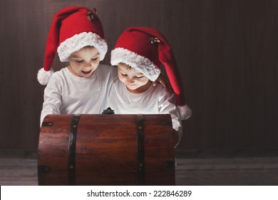 Two adorable boys, opening wooden chest, glowing light from inside, happy kids with santa hats - Powered by Shutterstock