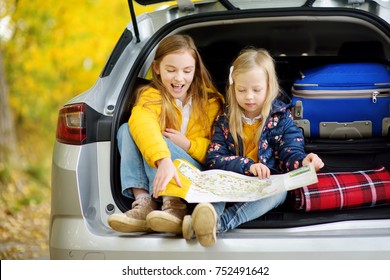 Two Adorable Girls Sitting In A Car Trunk Before Going On Vacations With Their Parents. Two Kids Looking Forward For A Road Trip Or Travel. Autumn Break At School. Family Travel By Car.