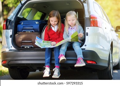 Two adorable little girls ready to go on vacations with their parents. Kids sitting in a car examining a map. Traveling by car with kids. 