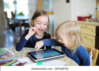 Two adorable little sisters playing with a digital tablet at home - Powered by Shutterstock