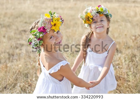 Two adorable little sisters wearing flowers crowns by warm and sunny summer day