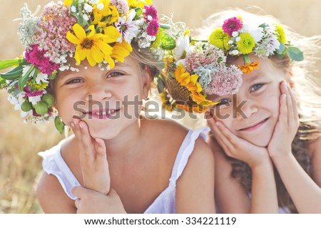 Two adorable little sisters wearing flowers crowns by warm and sunny summer day