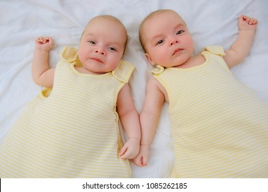 Two Adorable Twin Babies Lying Down On White Sheet In Yellow Sleeping Sacks Ready To Go To Bed. Safe Sleep For Babies. Infants In Wearable Blankets