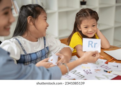 Two adorable young Asian girls are enjoying studying English alphabet flashcards with a private teacher at home. preschool, kindergarten, elementary school