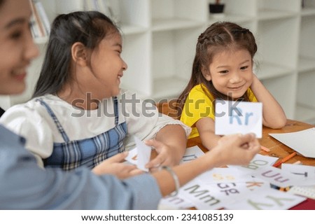 Two adorable young Asian girls are enjoying studying English alphabet flashcards with a private teacher at home. preschool, kindergarten, elementary school