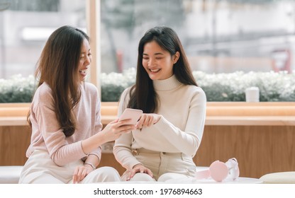 Two Adorable Young Long Hair Women Wearing Sweater, Chatting Together, Holding Mobile Phone, Smiling With Happiness, Sitting In Cafe Coffee Shop In Winter Season With Comfortable. Lifestyle Concept