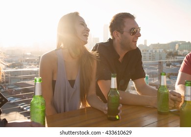 Two Adult Friends Drinking Beer At Rooftop Bar Table With Los Angeles Skyline, USA