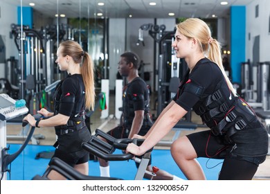 Two adult girls dressed EMS vests friendly talking while training in fitness gym
