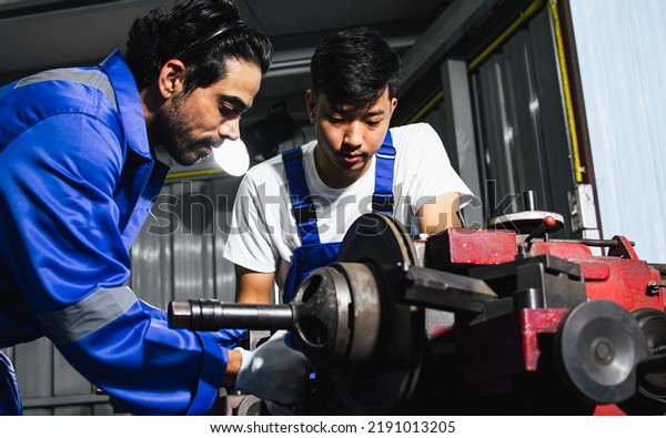 Two adult handsome male mechanics wearing\
uniform, using machine for fix, repair car or automobile\
components, teamwork helping, working in car maintenance service\
center or shop. Industry\
Concept