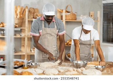 Two adult male bakers cutting dough with scraper and rolling it out with rolling pin - Powered by Shutterstock