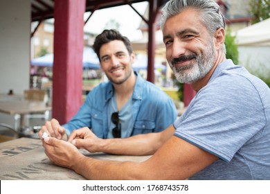 Two Adult Male Friends Sit Talking Over Coffee Outside Cafe