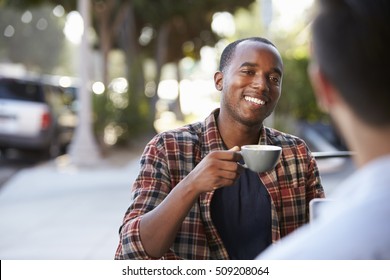 Two Adult Male Friends Sit Talking Over Coffee Outside Cafe