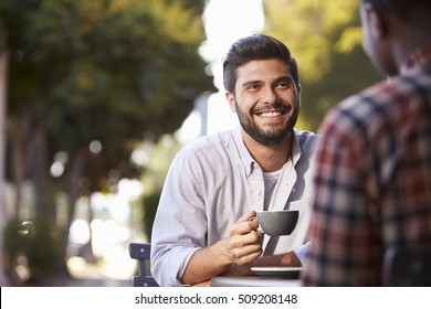 Two Adult Male Friends Sit Talking Over Coffee Outside Cafe