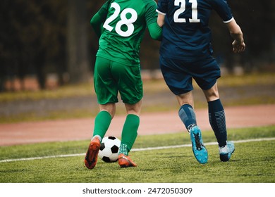 Two Adult Soccer Football Players Compete For Ball Next To Pitch Sideline. Soccer Players in Green And Blue Team In a Duel. Footballers in Jersey Uniforms - Powered by Shutterstock