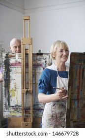 Two Adult Students Painting At Easels In Art Class