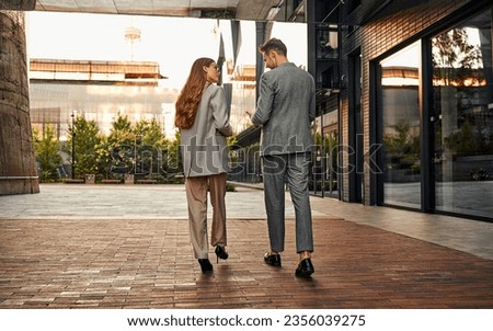 Two adult stylish people are walking around the business center and talking with their backs turned to the camera. Copy space.