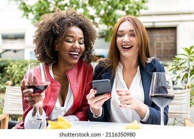 Two Adult Woman Having Fun During Happy Hour After Work, Colleagues Laughing While Looking At Smart Phone, Social Network And Mobile App For Tech Addicted People