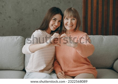 Two adult women mature mom young kid wear casual clothes show shape heart with hands heart-shape sign hug sit on gray sofa stay home flat rest relax spend free spare time in living room Family concept