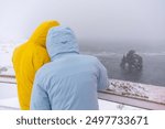 Two adventurers looking at the frozen rock figure of Hvitserkur in Icelandic winter