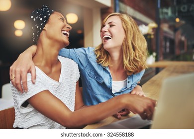 Two affectionate multiracial women friends hugging and laughing as they point at a laptop computer screen that they are sharing - Powered by Shutterstock