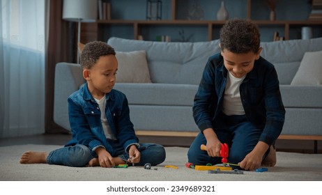 Two African American brothers little ethnic boys children siblings friends kids at home floor in living room playing with toy tools repairing building with hammer having fun busy play game with toys - Powered by Shutterstock