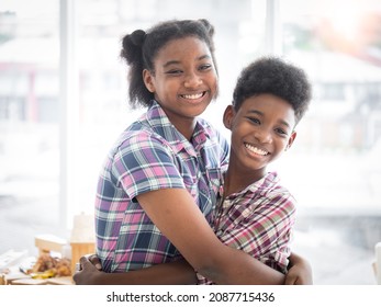 Two African American brothers and sisters hug the neck and look camera's smile. Older sister hugs little brother by the neck - Shutterstock ID 2087715436