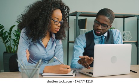 Two African American Business People Working Together In In The Office. African American Businessman And Businesswoman Talking, Using Laptop And Writing Down Information. Business Team