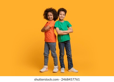 Two African American children, a boy and a girl, are standing confidently back to back with arms crossed on chest in front of a bright yellow background. - Powered by Shutterstock