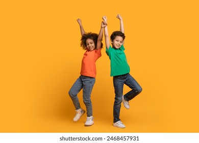 Two African American children, one wearing a red shirt and the other in a blue shirt, are energetically jumping on a vibrant yellow background - Powered by Shutterstock