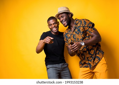 Two African American Friends Guys In Summer Clothes Are Smiling Broadly And Laughing Looking At The Camera And Pointing With Their Fingers