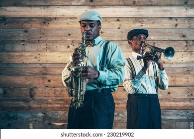 Two African American Jazz Musicians Playing Trumpet And Saxophone. Standing In Front Of Old Wooden Wall.