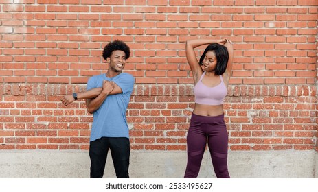 Two African American people stretching against a brick wall. Both African American are wearing athletic clothing. African American people preparing for exercise. African American couple stretching. - Powered by Shutterstock