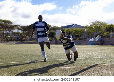 Two African American young male athletes in striped jerseys play rugby under the sun on a field. Both have short hair, and one is passing the ball while running. - Powered by Shutterstock