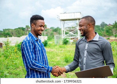 two african business men shake hands, smiling