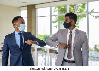 Two African Businessman Wearing Medical Mask While Greeting With Elbow Bump Greeting At Office. Social Distance Concept During The Coronavirus Epidemic.