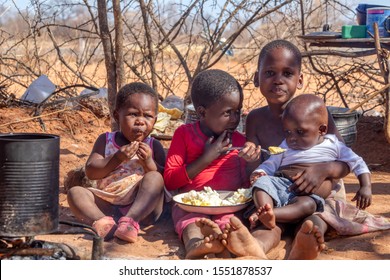 two african children in a village near Kalahari desert, the sister feeding her brother in the outdoors kitchen