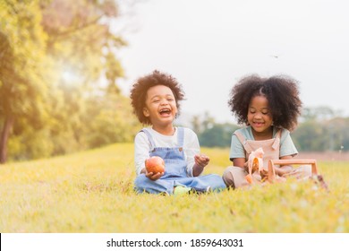 Two African Dark Skin Child Boy And Girl Sitting And Eating Fruits In Parks And Outdoors With Happy. African Child Boy And Girl Eating Apple And Banana With Smile In Grass Field Tropical Autumn.