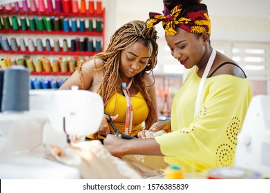 Two african dressmaker woman sews clothes on sewing machine and work with scissors at tailor office. Black seamstress girls. - Powered by Shutterstock