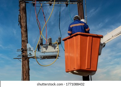 Two African Electrician On The Orange Basket Of A Crane On The Pole